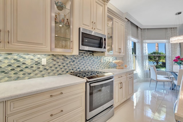 kitchen with tasteful backsplash, cream cabinets, decorative light fixtures, light tile patterned floors, and appliances with stainless steel finishes