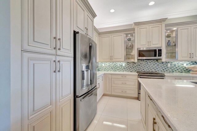 kitchen with light stone countertops, tasteful backsplash, appliances with stainless steel finishes, light tile patterned floors, and ornamental molding