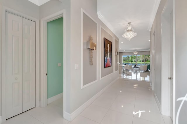 hall with light tile patterned floors, ornamental molding, and a notable chandelier