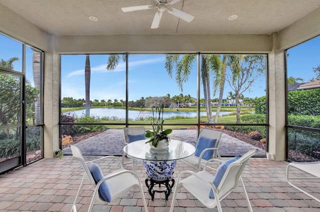 sunroom with ceiling fan and a water view