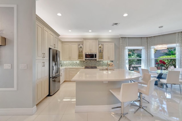 kitchen with decorative backsplash, appliances with stainless steel finishes, pendant lighting, cream cabinetry, and light tile patterned flooring