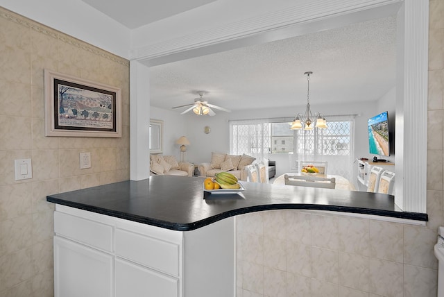 kitchen with tile walls, white cabinetry, a textured ceiling, ceiling fan with notable chandelier, and hanging light fixtures