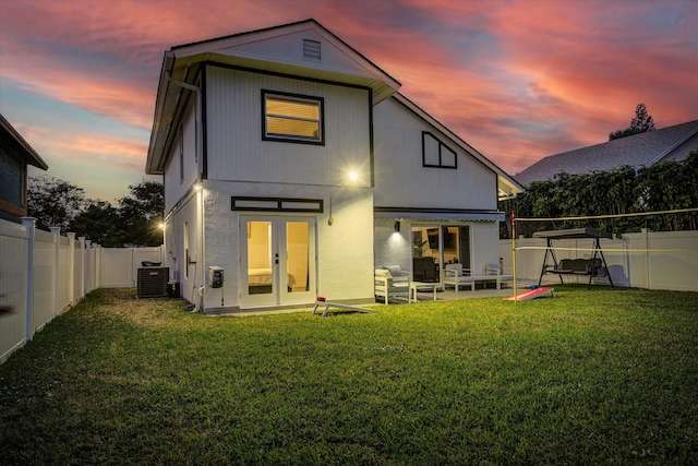 back house at dusk with a patio, central air condition unit, french doors, and a yard