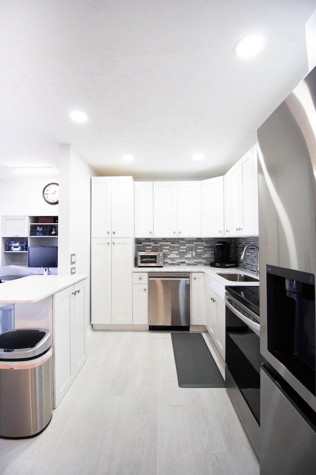 kitchen with backsplash, sink, appliances with stainless steel finishes, light hardwood / wood-style floors, and white cabinetry