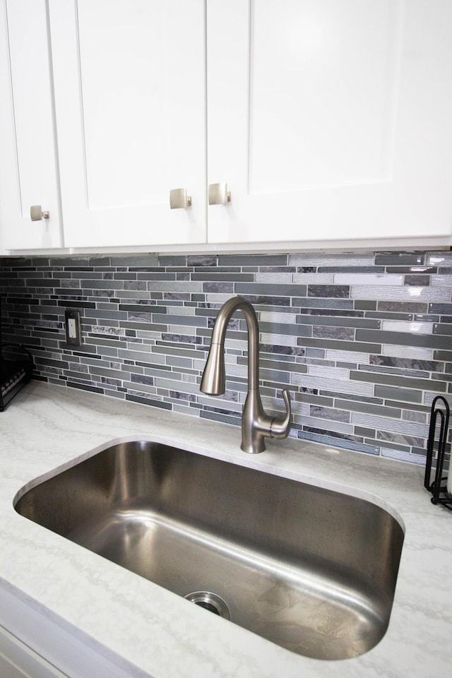 details with white cabinets, tasteful backsplash, light stone counters, and sink