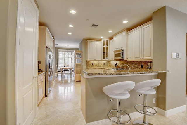 kitchen featuring stainless steel appliances, light stone counters, kitchen peninsula, decorative backsplash, and light tile patterned flooring