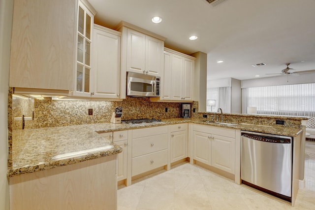 kitchen with ceiling fan, sink, stainless steel appliances, light stone counters, and kitchen peninsula