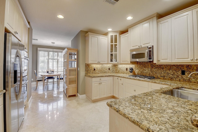 kitchen with light stone countertops, appliances with stainless steel finishes, tasteful backsplash, sink, and decorative light fixtures