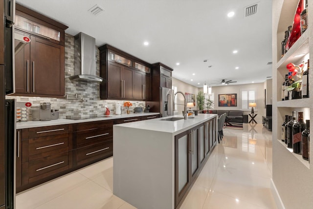 kitchen featuring a center island with sink, wall chimney range hood, sink, ceiling fan, and light tile patterned flooring