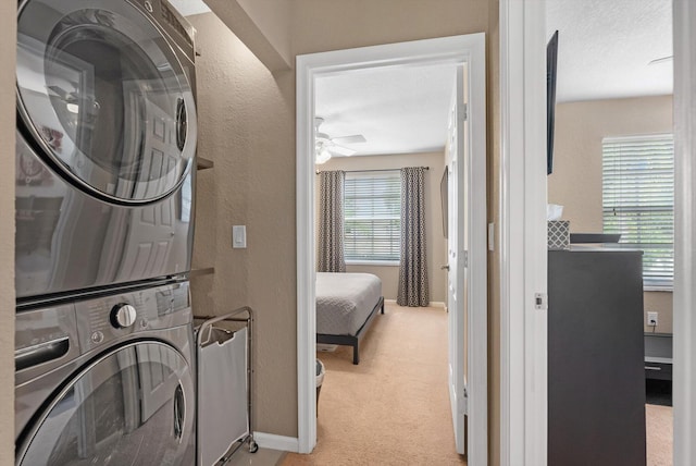 laundry room featuring ceiling fan, light colored carpet, stacked washing maching and dryer, and a textured ceiling