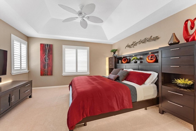 carpeted bedroom with ceiling fan, a raised ceiling, and multiple windows