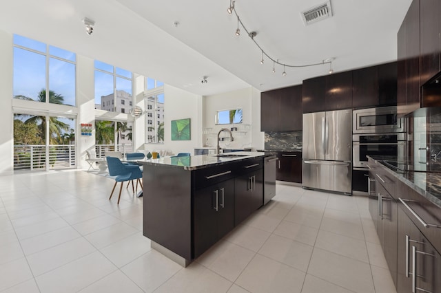 kitchen with appliances with stainless steel finishes, tasteful backsplash, light tile patterned floors, and a center island with sink