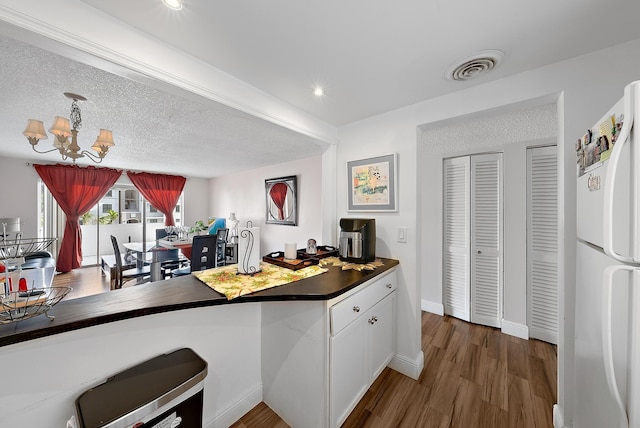 kitchen featuring white cabinetry, dark hardwood / wood-style flooring, white refrigerator, a chandelier, and a textured ceiling