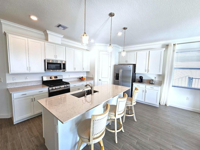 kitchen featuring appliances with stainless steel finishes, white cabinetry, pendant lighting, and an island with sink