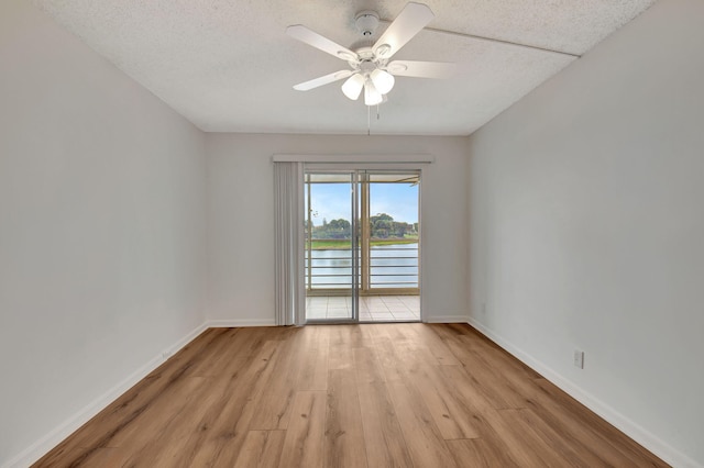 empty room featuring a textured ceiling, a water view, ceiling fan, and light hardwood / wood-style floors