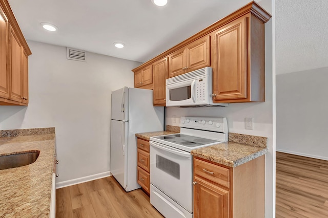 kitchen featuring light wood-type flooring, white appliances, light stone counters, and sink