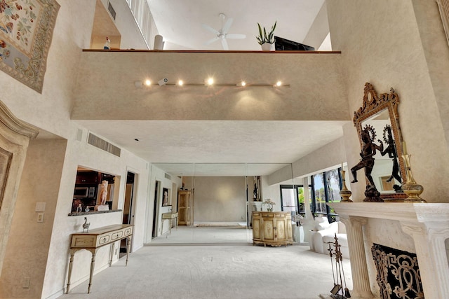 living room featuring ceiling fan, light colored carpet, a towering ceiling, and a fireplace