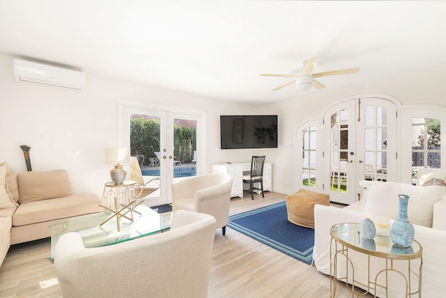 living room with a wall mounted AC, ceiling fan, french doors, and light wood-type flooring