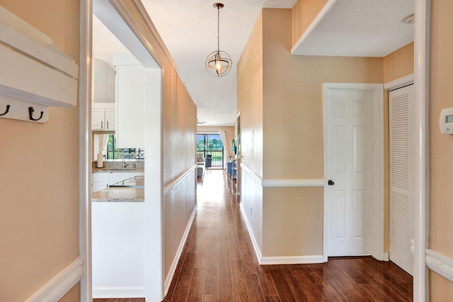 corridor with dark hardwood / wood-style floors, sink, a textured ceiling, and an inviting chandelier