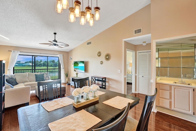 dining area with sink, dark wood-type flooring, high vaulted ceiling, a textured ceiling, and ceiling fan with notable chandelier