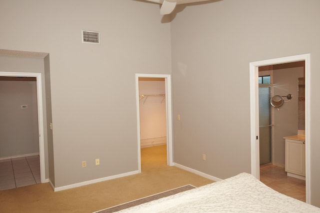 unfurnished bedroom featuring light carpet, ensuite bathroom, ceiling fan, a spacious closet, and a closet