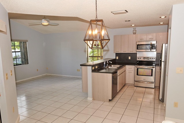 kitchen with kitchen peninsula, ceiling fan with notable chandelier, stainless steel appliances, sink, and hanging light fixtures