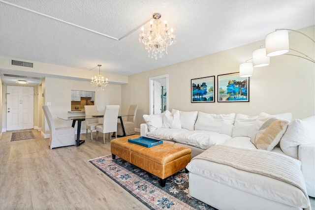 living room with a textured ceiling, light wood-type flooring, and a notable chandelier