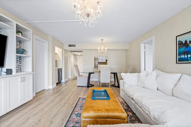 living room with washer / dryer, a chandelier, a textured ceiling, and light wood-type flooring