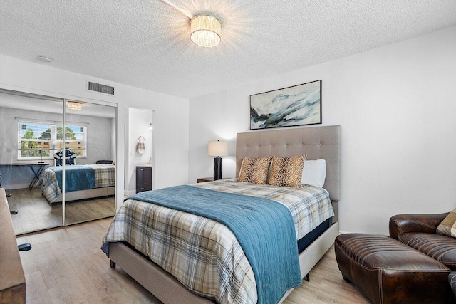 bedroom featuring a textured ceiling, ensuite bath, light hardwood / wood-style flooring, and a closet