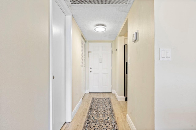 hall with light wood-type flooring and a textured ceiling