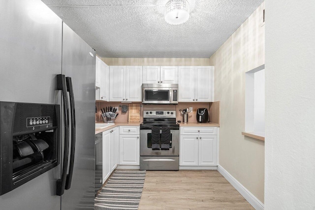 kitchen with white cabinetry, light hardwood / wood-style floors, a textured ceiling, and appliances with stainless steel finishes