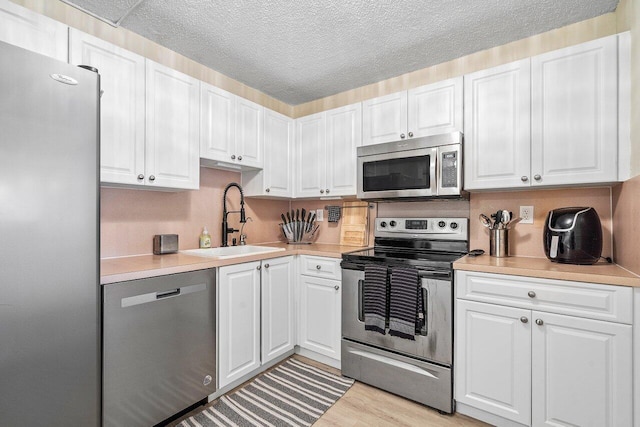 kitchen featuring sink, stainless steel appliances, light hardwood / wood-style flooring, a textured ceiling, and white cabinets