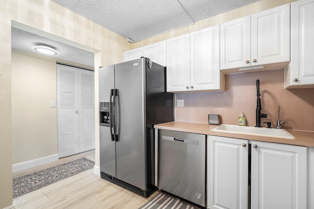 kitchen with a textured ceiling, stainless steel appliances, sink, white cabinets, and light hardwood / wood-style floors