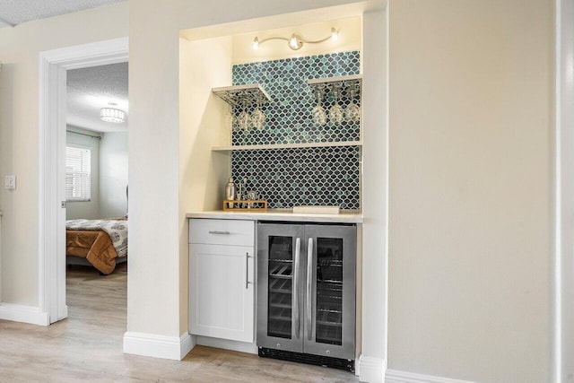 bar with white cabinets, light hardwood / wood-style floors, a textured ceiling, and wine cooler