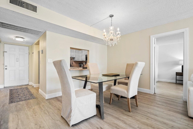 dining room featuring light hardwood / wood-style floors, a textured ceiling, and an inviting chandelier