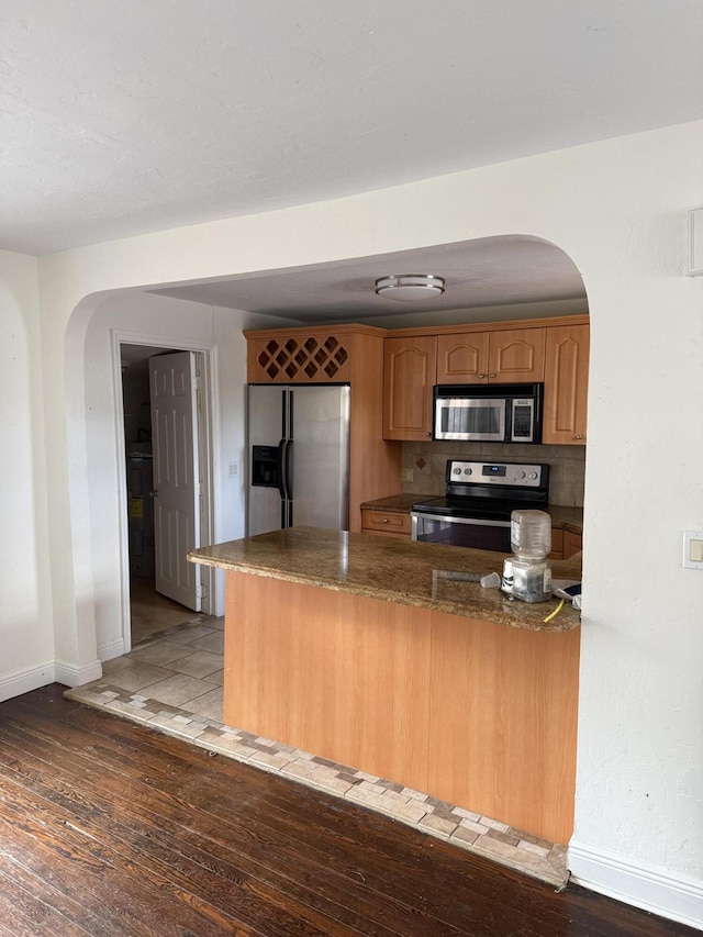 kitchen with kitchen peninsula, decorative backsplash, light hardwood / wood-style floors, and appliances with stainless steel finishes