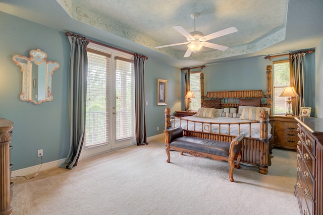 carpeted bedroom with a raised ceiling, multiple windows, ceiling fan, and access to outside