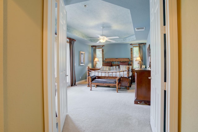 bedroom featuring a textured ceiling, light carpet, and a tray ceiling