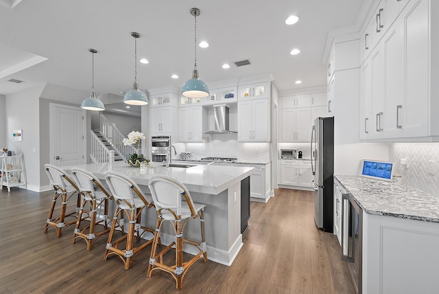 kitchen with white cabinets, hanging light fixtures, wall chimney exhaust hood, a large island, and stainless steel appliances