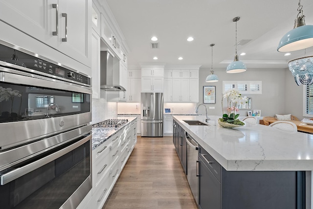 kitchen with pendant lighting, a kitchen island with sink, wall chimney exhaust hood, white cabinetry, and stainless steel appliances