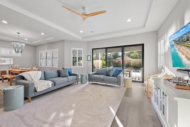 living room featuring a tray ceiling, light hardwood / wood-style flooring, and ceiling fan with notable chandelier