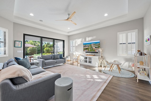 living room featuring wood-type flooring, a raised ceiling, and ceiling fan