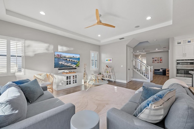 living room featuring hardwood / wood-style floors, a tray ceiling, and ceiling fan