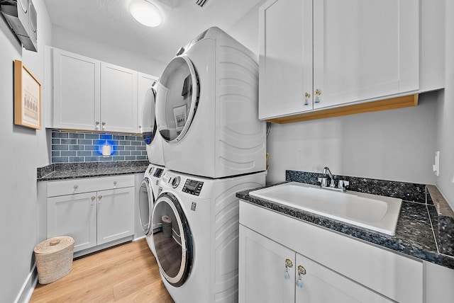 laundry area with cabinets, light wood-type flooring, a textured ceiling, sink, and stacked washer / dryer