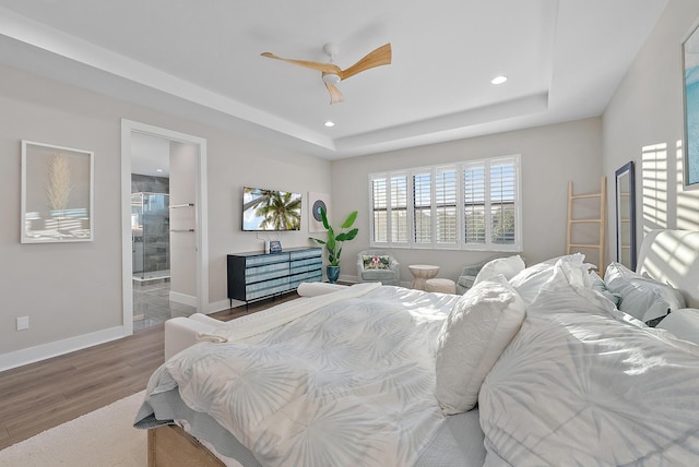 bedroom featuring wood-type flooring, connected bathroom, a tray ceiling, and ceiling fan