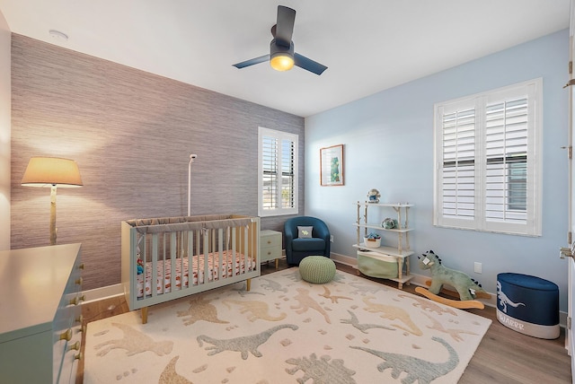 bedroom with hardwood / wood-style floors, ceiling fan, and a nursery area