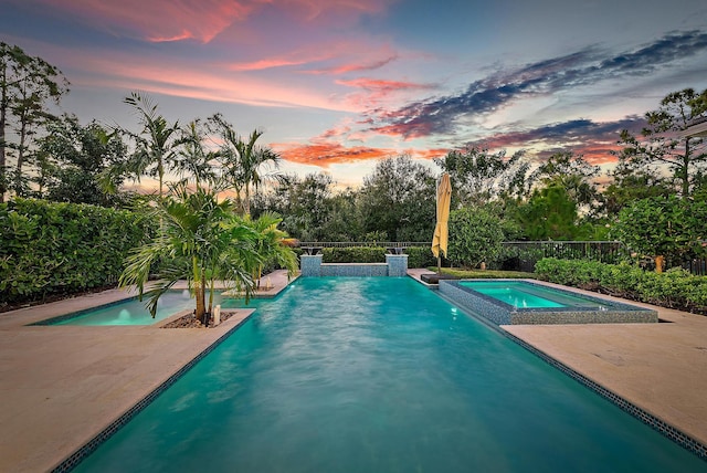 pool at dusk featuring an in ground hot tub and a patio