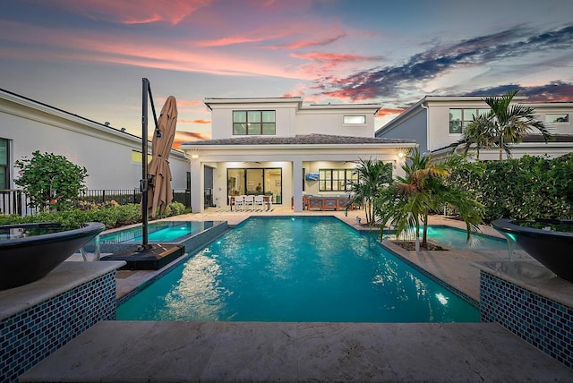 back house at dusk featuring a patio area and a swimming pool with hot tub