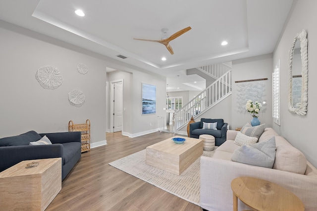 living room with a raised ceiling, ceiling fan, and hardwood / wood-style flooring