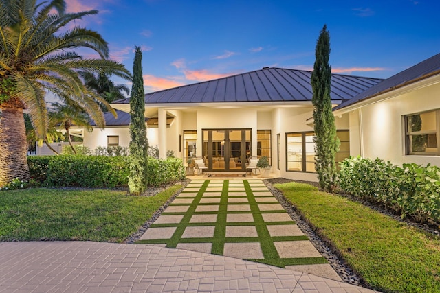 back house at dusk featuring a yard and french doors